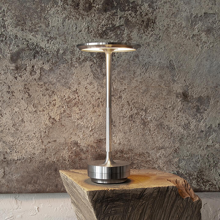 Silver cordless table lamp on a rustic wood block against a concrete wall