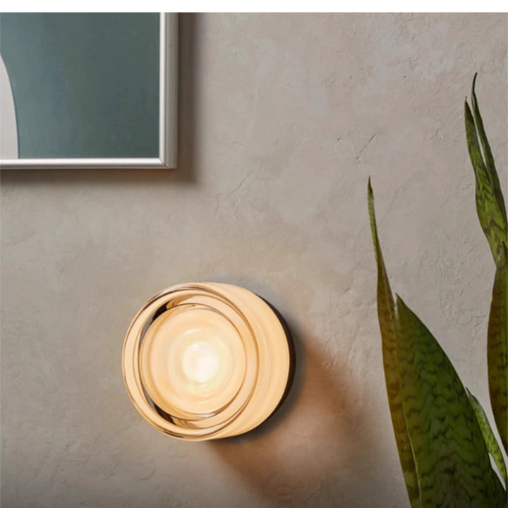 Amber Ripple Glass Surface Mount Light lit on a textured plaster wall beside a plant